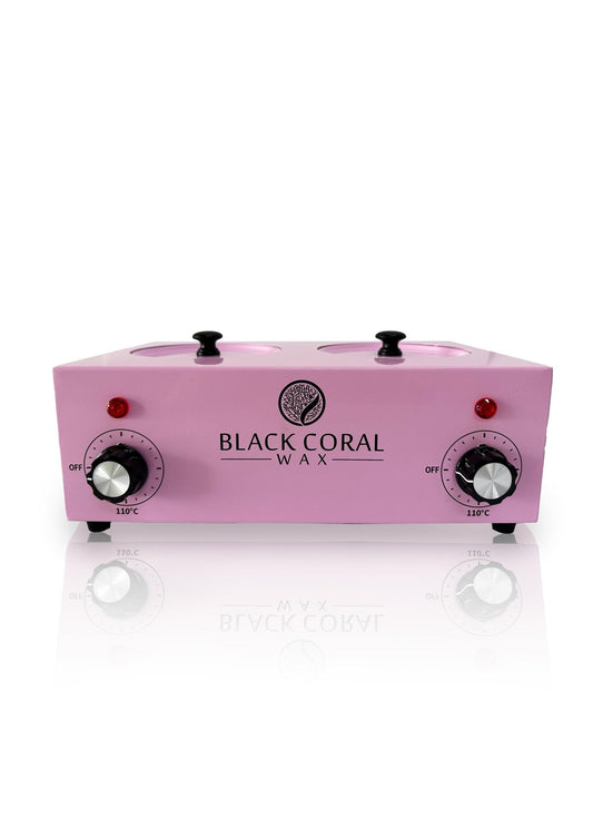 The Black Coral Wax USA Double (2x1lb) Wax Warmer is pink with two pots, silicone inserts, temperature control dials, power switches, and indicator lights on the front panel. The brand logo appears in black between the controls.