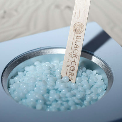 Blue wax beads in a container with a wooden spatula labeled 'Black Core Wax'.