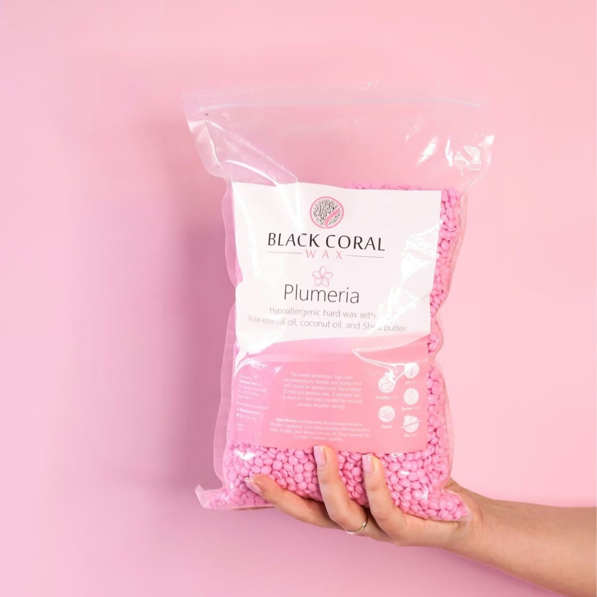 Bag of pink wax beads labeled 'Black Coral Wax Plumeria' held against a pink background