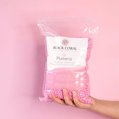 Bag of pink wax beads labeled 'Black Coral Wax Plumeria' held against a pink background