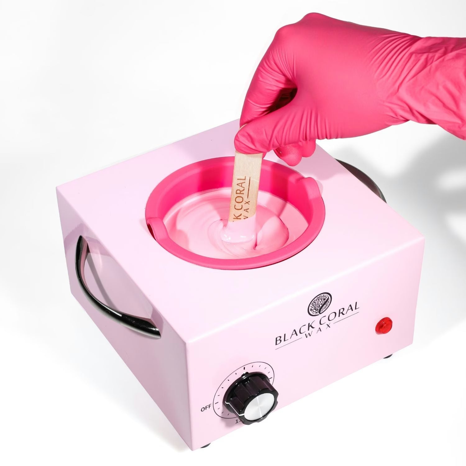 Pink wax warmer with a hand wearing a pink glove dipping a wooden stick into melted wax, branded 'Black Coral'.